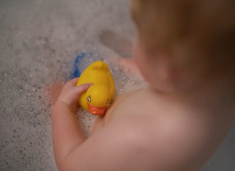 beba se kupa u kadi i drži igračke u ruci